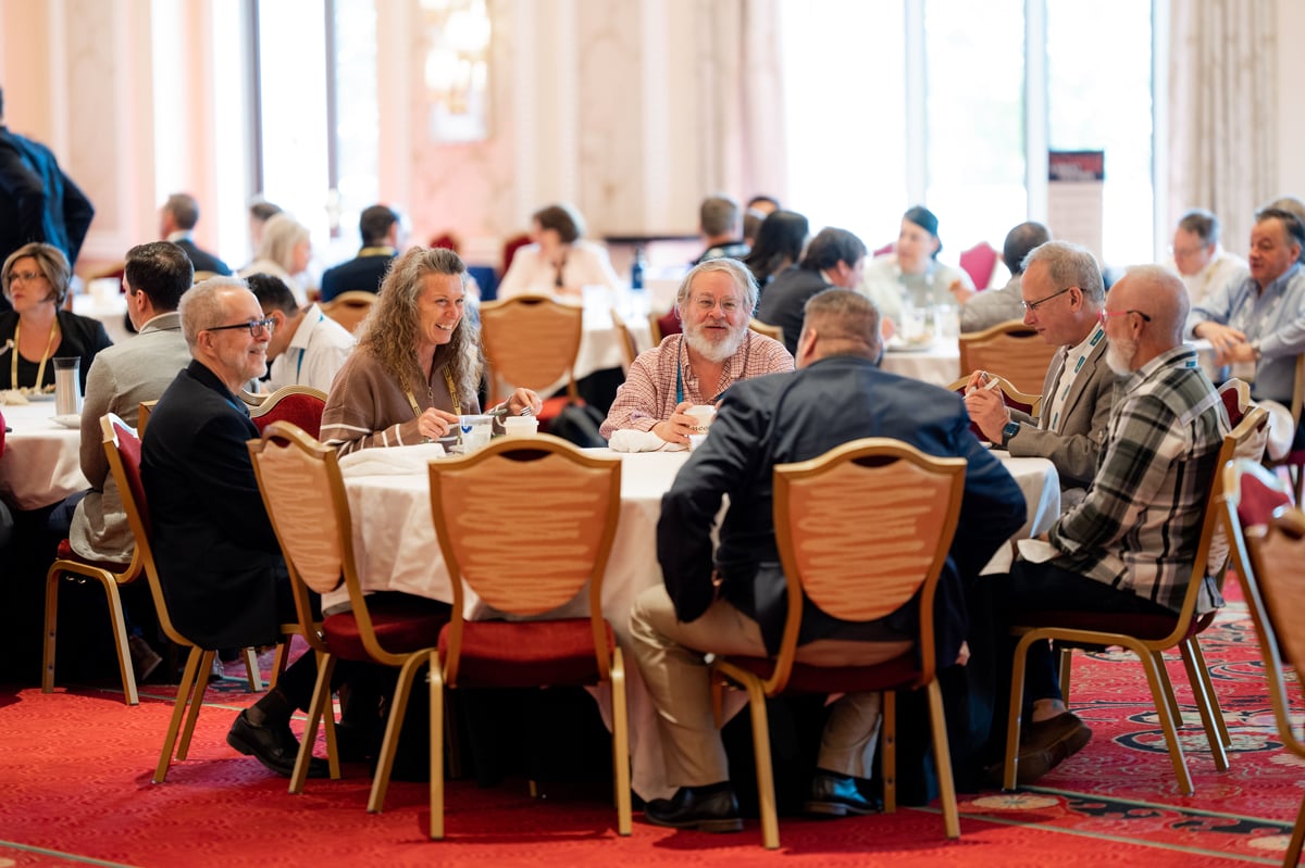A full ballroom of attendees in discussion at round tables